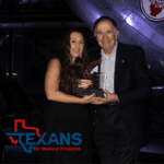Woman and man holding an eagle award with an American flag, with the Texans for Medical Freedom logo.